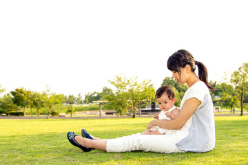 緑の芝生の上に座りくつろぐ赤ちゃんとお母さん親子