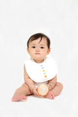 白背景で座り正面を向くカメラ目線の女の子の赤ちゃん