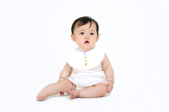 白背景でお座りする女の子の赤ちゃん。成長,健康,元気,育児イメージ