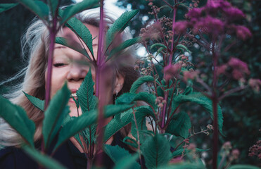 Senior blonde woman smiles freely, hiding among meadow flowers, expressing naturalness and freedom. woman smiling 50-60s