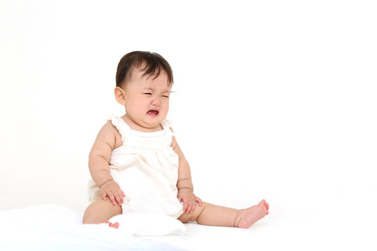 白背景でお座りする女の子の赤ちゃん。成長,健康,元気,育児イメージ