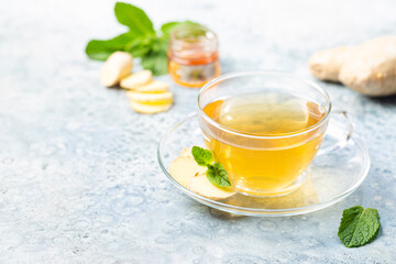 Ginger tea in a glass cup with lemon and mint on light background