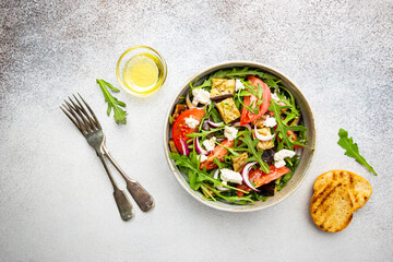 Eggplant salad with tomatoes, arugula and feta cheese in a bowl on white background, top view