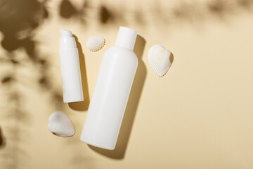 Set of white cosmetic bottles and jars with seashells on a beige background with hard shadows. The concept of beauty salon and summer cosmetics for tanning