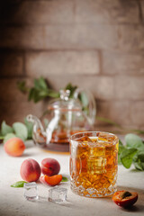 Glass of peach or apricot iced tea with fruit slices against white background