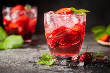 Refreshing summer drink with strawberry slices in glasses on dark background