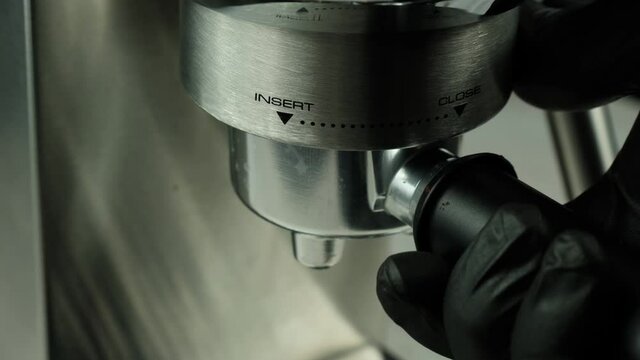 The process of installing the portafilter with ground coffee in the espresso machine. Professional coffee shop worker installing portafilter to prepare aromatic black coffee in an espresso machine. 