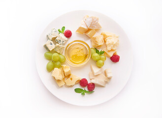 A plate with five kinds of cheese, grapes, fresh raspberries and honey. Top view on white background