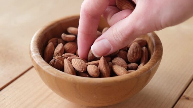 Hand picking almond nut from a wooden bowl. Eating nuts. Healthy vegan snack food