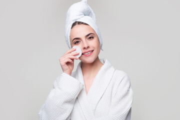 Woman in spa towel using face cream and cotton pad isolated over gray background.