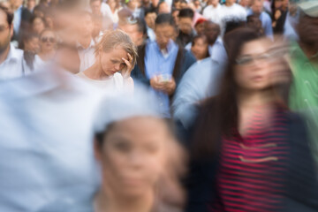 Obraz premium Crowd of people walking on city street - motion blurred image with unrecognizable faces - Young woman standing still, feeling down, depressed