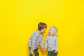 Two beautiful boys show each other tongues and have fun on a yellow background