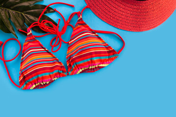 Women's red swimsuit and red hat flatlay composition on blue background. Top view. Place for text.