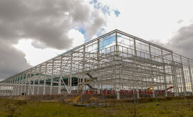 Metal framework of a partially fabricated large warehouse under construction. Landscape image with space for text. Overcast, clouded skyline. Oxfordshire, England. - 431571962