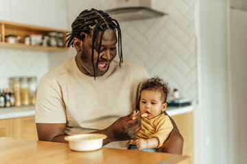 Happy dad feeding his baby daughter at home, portrait.