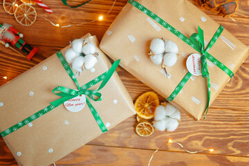 Top view of Christmas gifts on wooden table. Boxes in wrapping paper tied with ribbons with snowflakes. Toy soldier, dried oranges, garland and cotton in background. New year's atmosphere.
