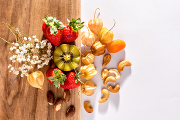 Kiwi, strawberries, cashews, Brazil nuts and physalis on wooden background. Top view.