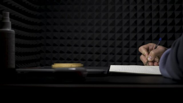 Concept of songwriting, side view of a man writing lyrics in a professional music studio. HDR. Process of creating a song by the author, musician writing text on a sheet of paper.