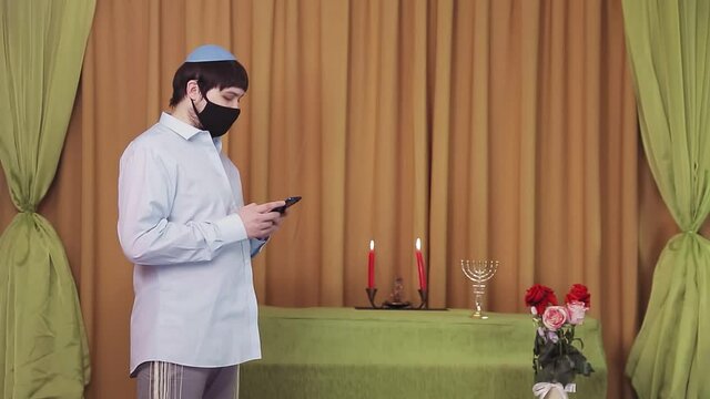 Before the chuppah ceremony, a Jewish groom in a protective mask in a synagogue hall dials an SMS by phone
