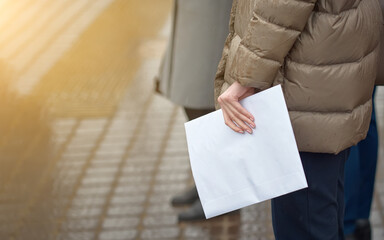 Female hand with manicure holding an envelope over street background. Person posting letter