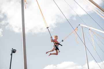 A girl of about 8 years old is jumping on a bungee trampoline. A child with a harness and elastic...