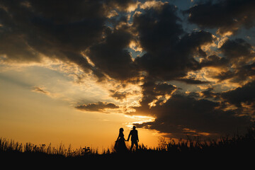 Silhouettes of man and woman walking along the plain on the background of a beautiful sunset sky 