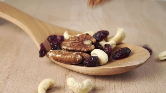 The ingredients of the nutty fruit mix fill the wooden spoon on the board. Falling pecans, cashews and raisins in slow motion. Close-up. Vitamin Protein Snack