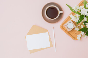 Mockup white greeting card and envelope with a cup of coffee and jasmine flowers on a color background