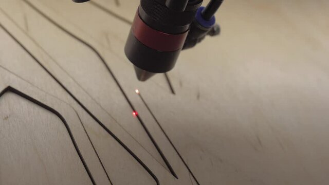 Industrial laser is cutting a pattern on a plywood sheet and moving slowly, close up. Modern wood burning with a laser. A red laser beam moves through a tree. No people. High quality footage