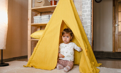 a little girl plays inside a yellow teepee