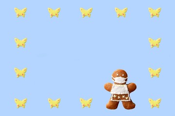 Cute gingerbread woman with protective face mask in a frame from butterflies, isolated, blue background. Greeting card, copy space for text. Creative concept in coronavirus (COVID-19) time