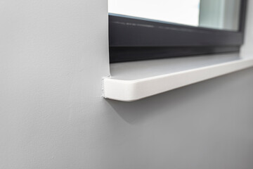 Newly installed white conglomerate window sill inside the room, on the gray wall.