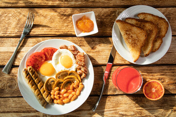 Traditional morning English breakfast - scrambled eggs, white beans, tomatoes, mushrooms, sausages and apricot jam with classic England fried toast on a white plate and red orange juice - top view