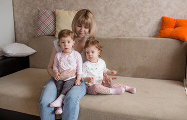 a loving mother sits on the couch and hugs her two young daughters.