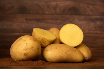 Raw ground-based potatoes on wooden table with potato split in half.