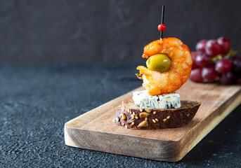 Single classic Spanish tapas lie on a wooden board. The tapas consist of shrimp, gorgonzola, green olive and bruschetta skewered for canapes - close-up