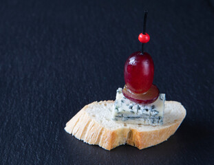 Classic tapas or bruschetta with gorgonzola cheese, red grapes, pierced for stability with a skewer on a baguette - a concept for dietary nutrition