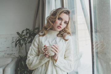 Young healthy woman relaxing and drinking coffee near window at home