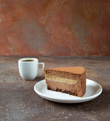 A piece of mousse French dessert - chocolate cake with a cup of espresso coffee for morning breakfast on a textured background - side view, close-up