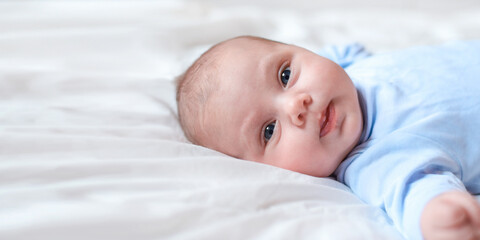 Close-up Portrait of a beautiful Baby on white. Head and Face. Newborn Baby lying on side and looks into the Camera. Motherhood, health, pediatrics concept. Banner. Cute adorable Infant. One month