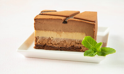 Delicious festive piece of mousse chocolate cake on a white square plate decorated with mint leaf - close-up