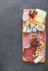Meat board with products from the Italian region to wine - sausages, cheeses, bread, fresh vegetables, green herbs, and grapes - top view and copy space