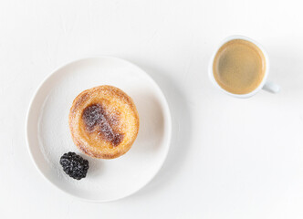 A cup of black coffee with the national dessert from Portugal - Pastel de nata, sprinkled with powdered sugar and blackberries for morning breakfast on a white background, top view