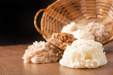 Cocada, Coconut candy from Brazil, white and brown cocadas fallen from a straw basket on wooden surface, black background, selective focus.
