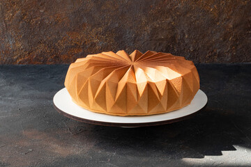 Modern chocolate mousse design cake covered with chocolate velour on the backing in the rays of sunlight and the reflection of a beautiful ornament on the table