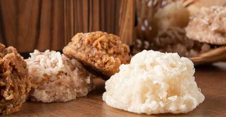 Cocada, Coconut candy from Brazil, white and brown cocadas fallen from a straw basket on wooden surface, selective focus.