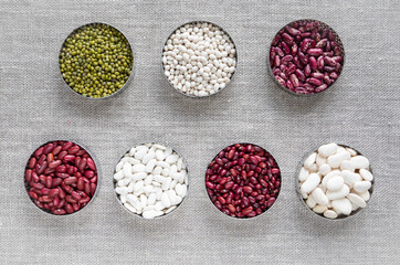 Various types of beans: colorful beans of different sizes in bowls on a table made of linen canvas - burlap - top view