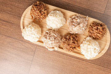 Fototapeta na wymiar Cocada, Coconut candy from Brazil, white and brown cocadas on wooden surface, black background, top view.