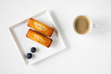 Traditional French dessert - financier cake pastries with blueberry on a white plate with a cup of...