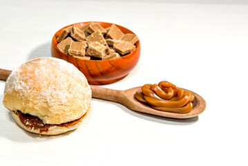 Dulce de leche candies with wooden spoon full of dulce de leche and Bread with cream, known as berlin ball, donut without a hole or 